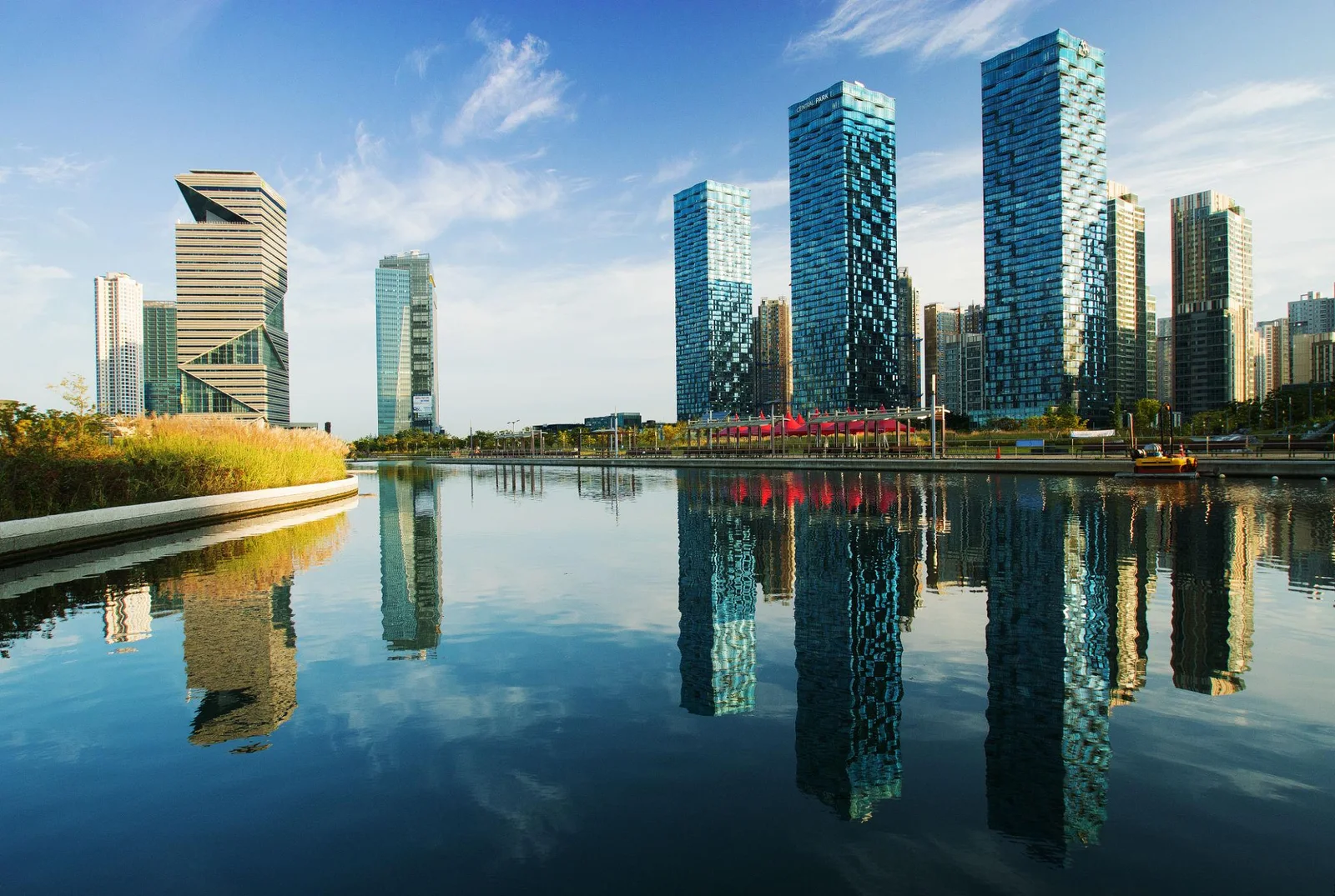 Modern towers reflected in water beside a landscaped urban park