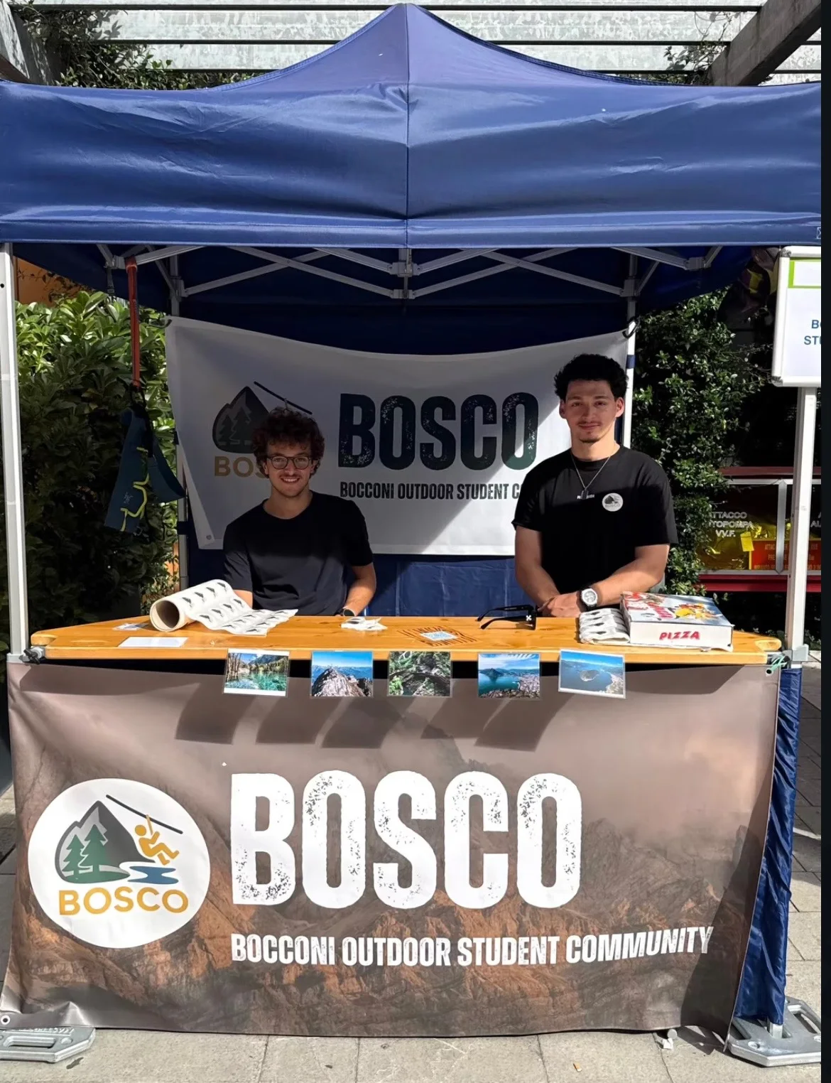 Two people behind a BOSCO community stand under a blue canopy